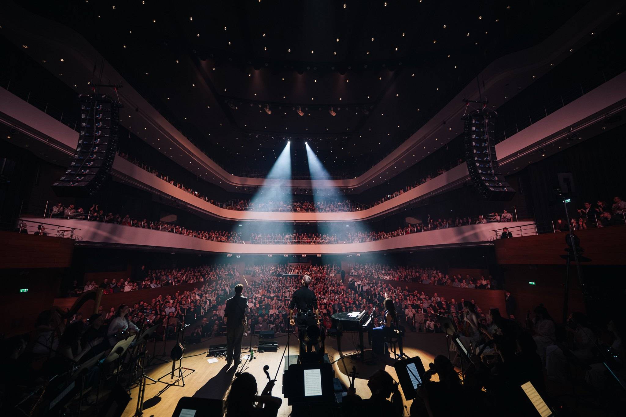 View from the balcony towards a concert hall stage, a beam of light over the audience