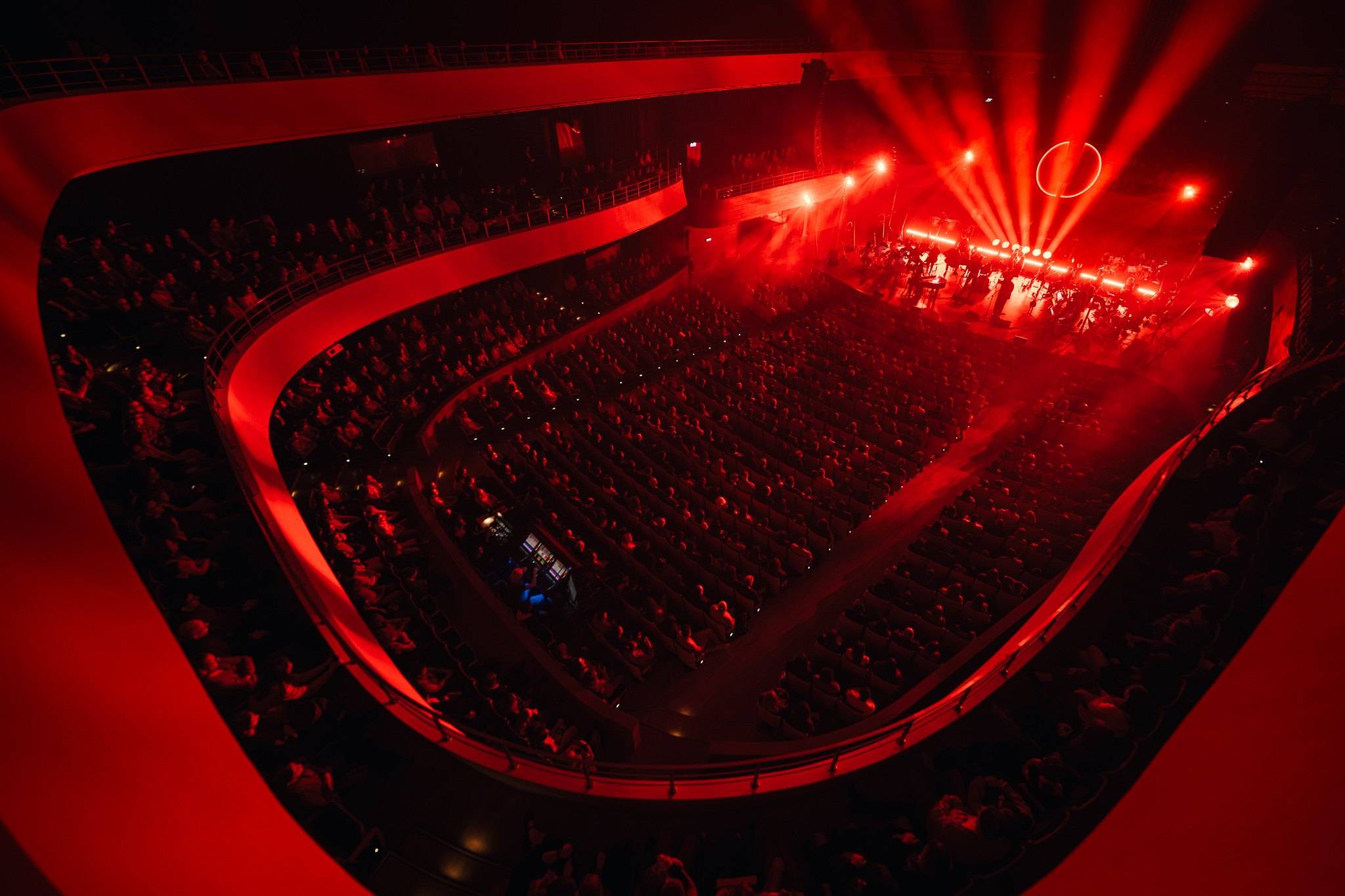 A concert in a hall with red balconies, stage lights above the stage