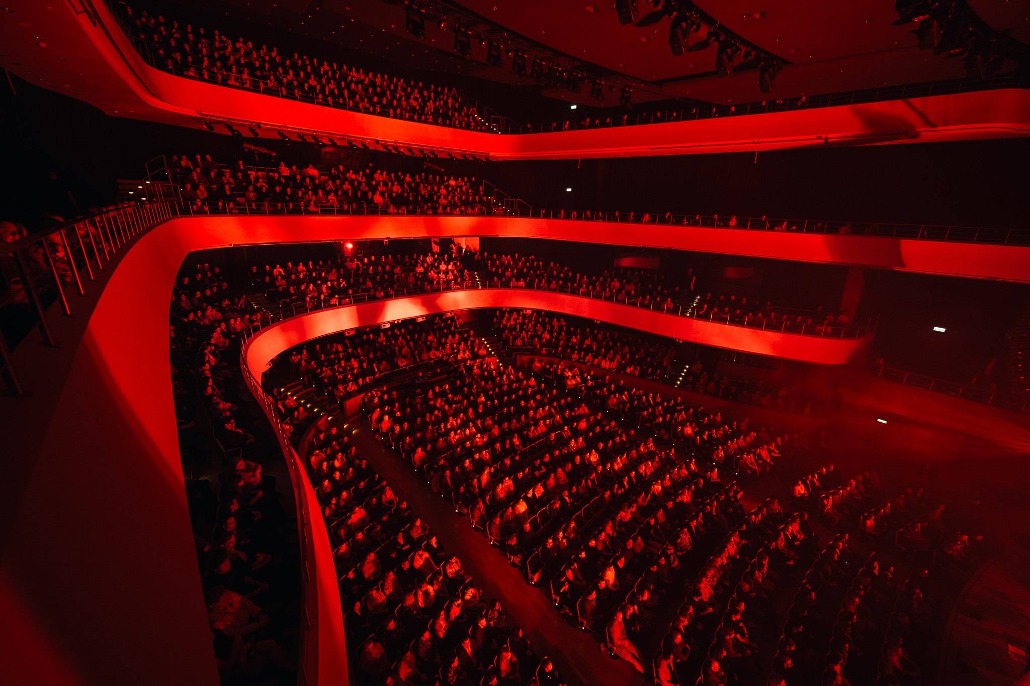 Concert hall in red light, seen from above over the balconies and audience
